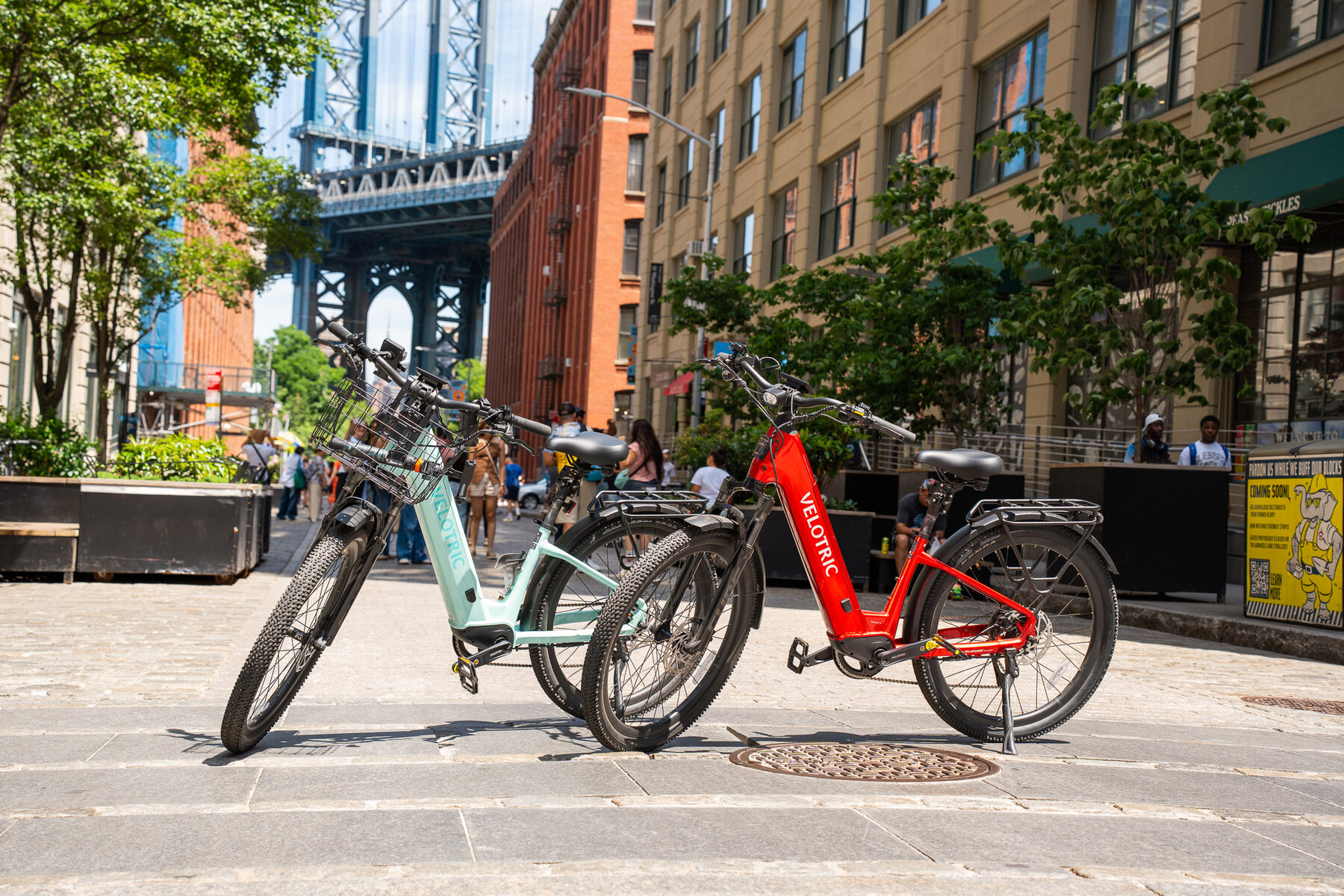 Velotric e-bikes on Washington Street DUMBO with Manhattan Bridge framed between Brooklyn warehouses — bike rental NYC ride from Midtown