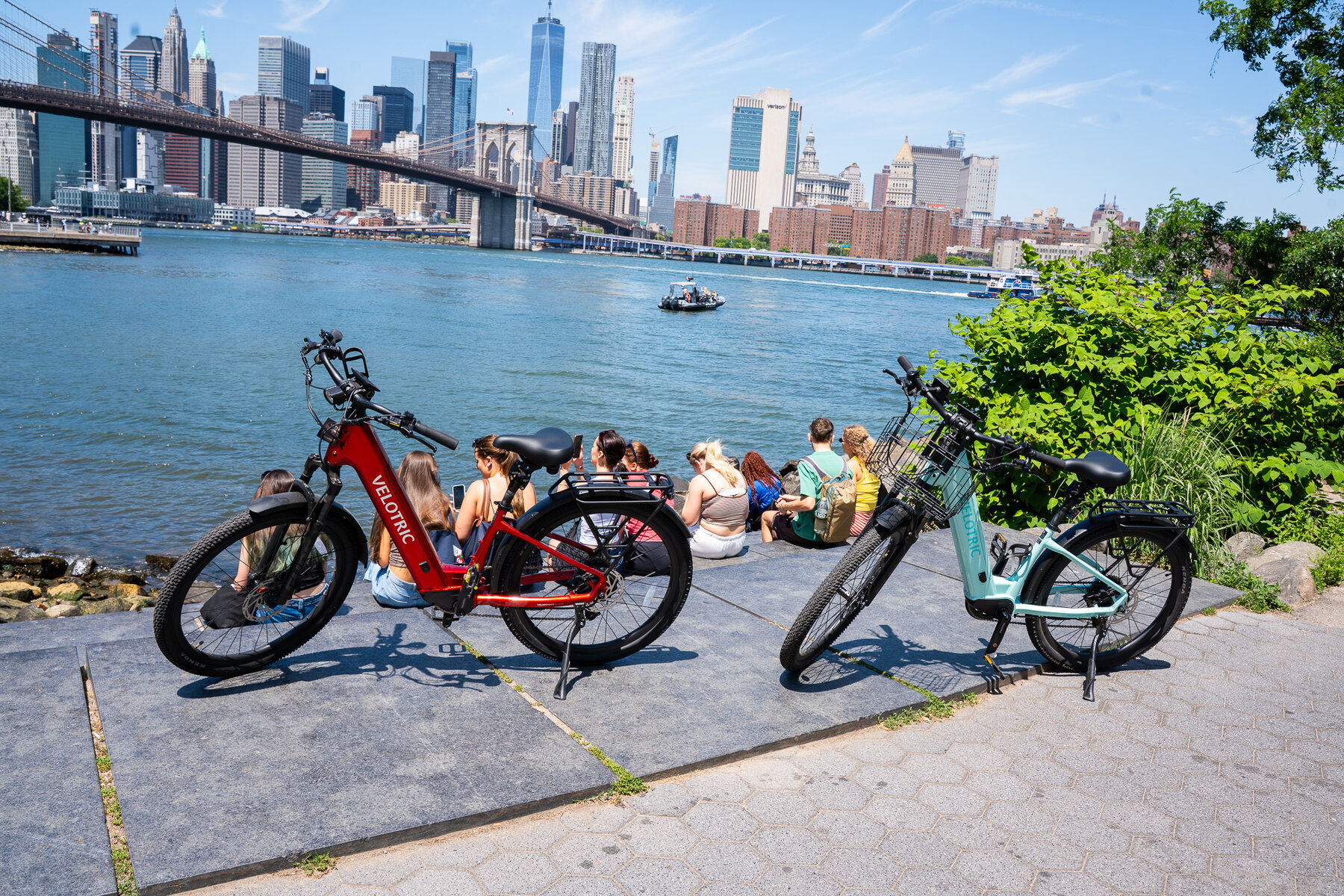 Velotric e-bikes at Brooklyn waterfront with Brooklyn Bridge and Manhattan skyline including One World Trade Center — historic NYC bike ride from Astra Bike Rentals